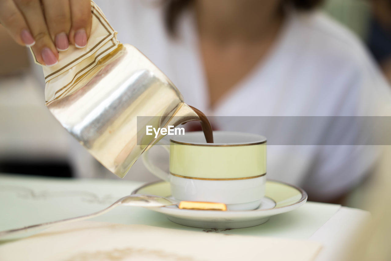 Midsection of woman pouring coffee in cup at home