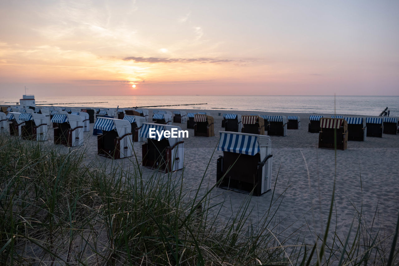 HOODED CHAIRS ON WOODEN POSTS AT BEACH AGAINST SKY