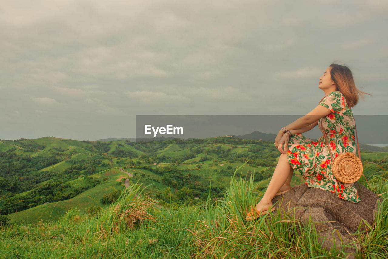 Woman sitting on land against sky