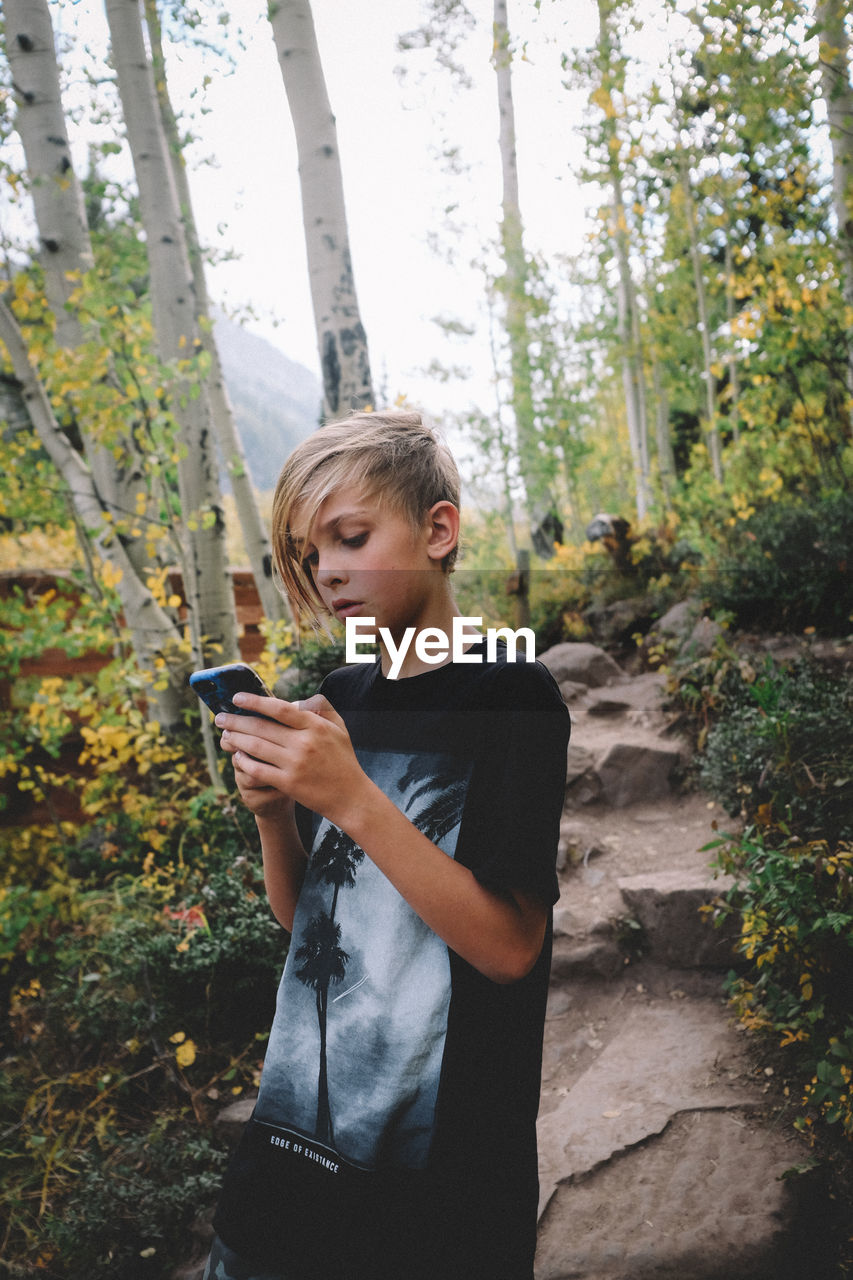 Tween boy checks phone while on a hike in colorado.