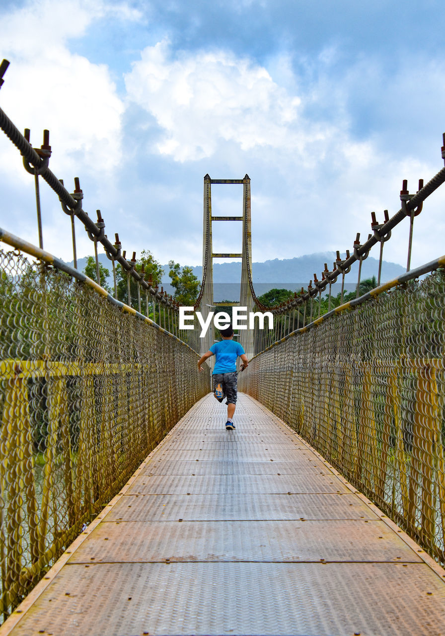 Rear view of boy walking on footbridge