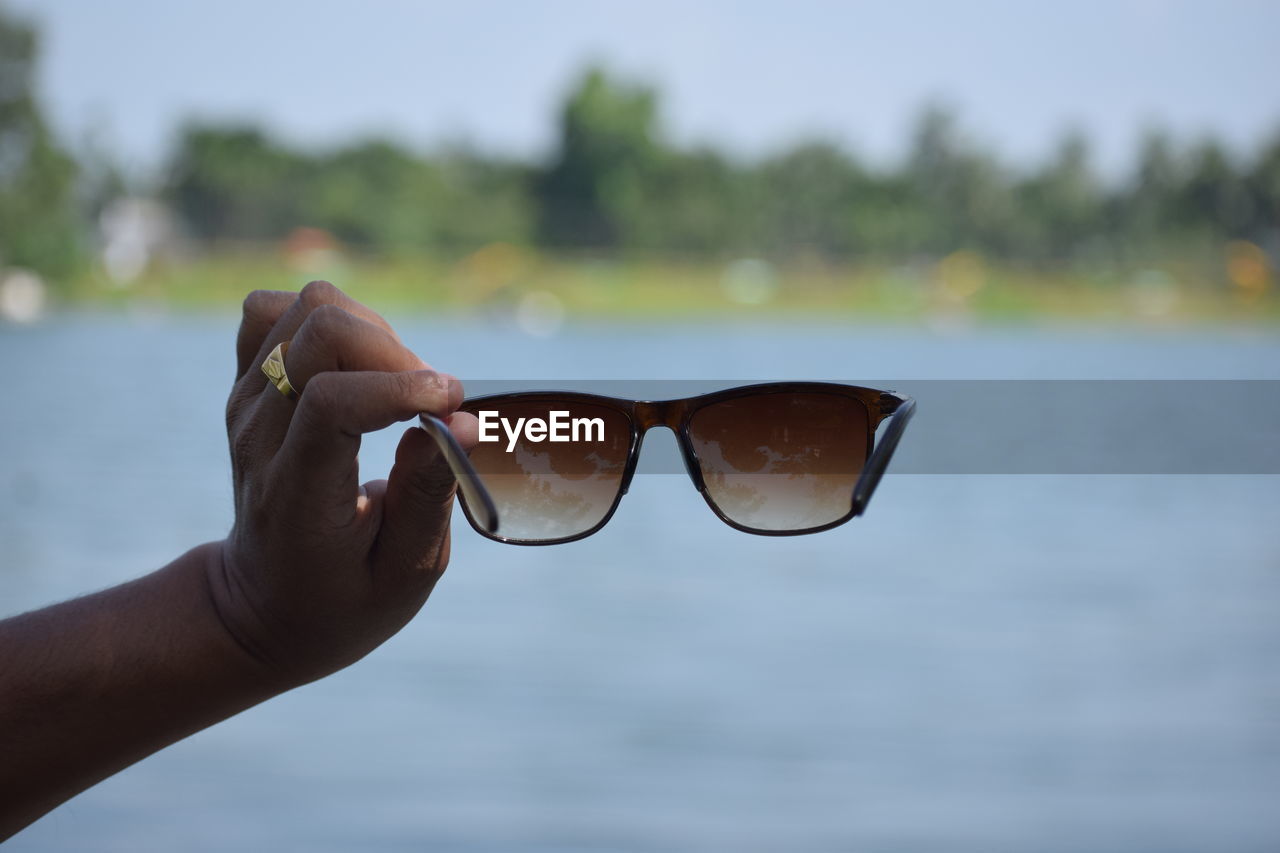 Cropped hand holding sunglasses against lake