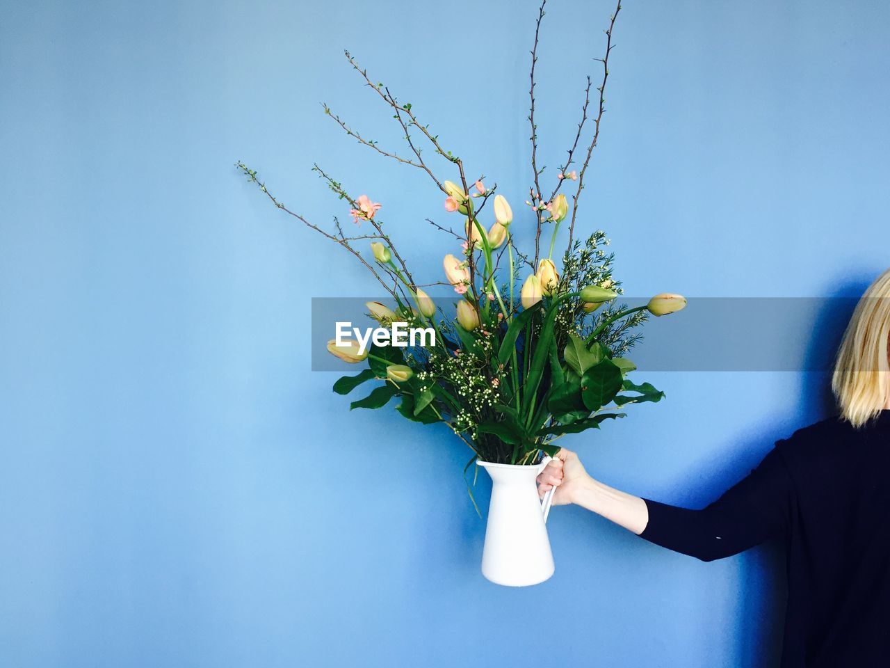 Cropped image of woman holding tulip vase against blue background