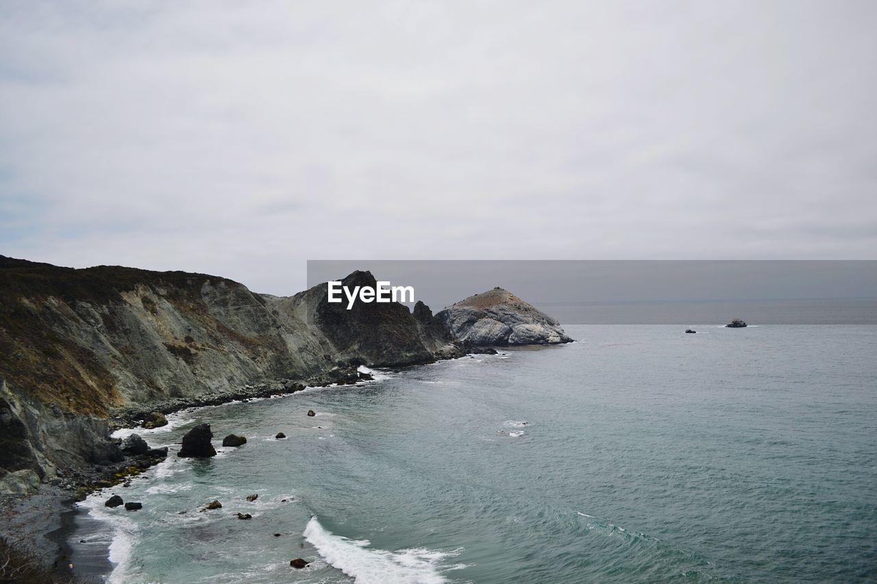 Scenic view of sea by cliff against cloudy sky