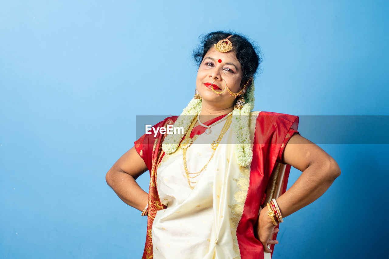 BEAUTIFUL YOUNG WOMAN LOOKING AWAY AGAINST BLUE BACKGROUND