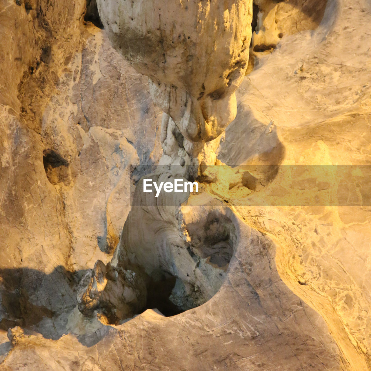 A gnome below a stalactite is an abstract dripstone shape on flowing stone in a cave wall.