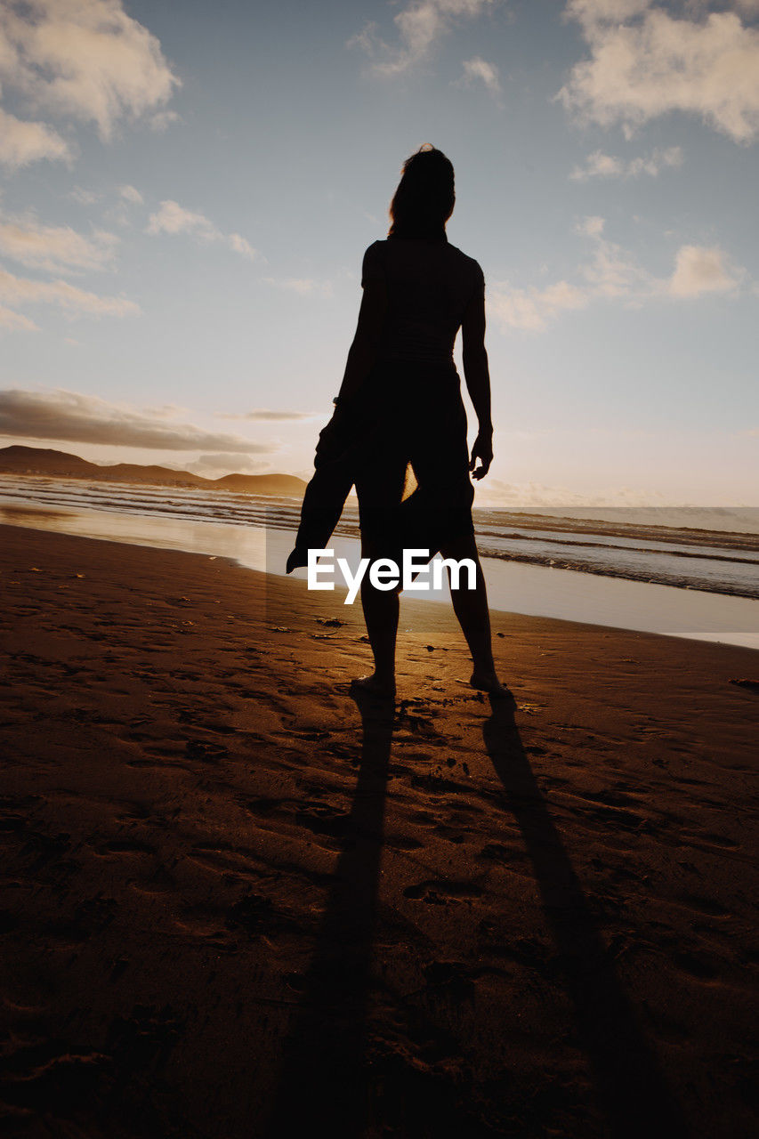 sky, land, beach, one person, horizon, full length, sea, nature, silhouette, water, sunset, adult, sunlight, sand, cloud, ocean, leisure activity, lifestyles, motion, men, holiday, standing, vacation, beauty in nature, trip, scenics - nature, sports, back lit, rear view, outdoors, person, solitude, coast, walking, travel, tranquility