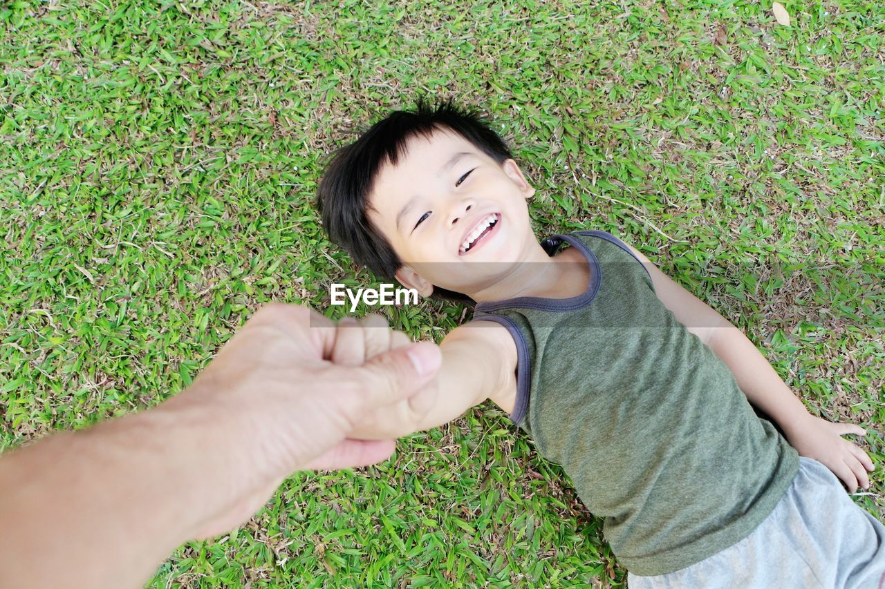 Little asian boy laying on the lawn happily and blurry hand of father takes care.
