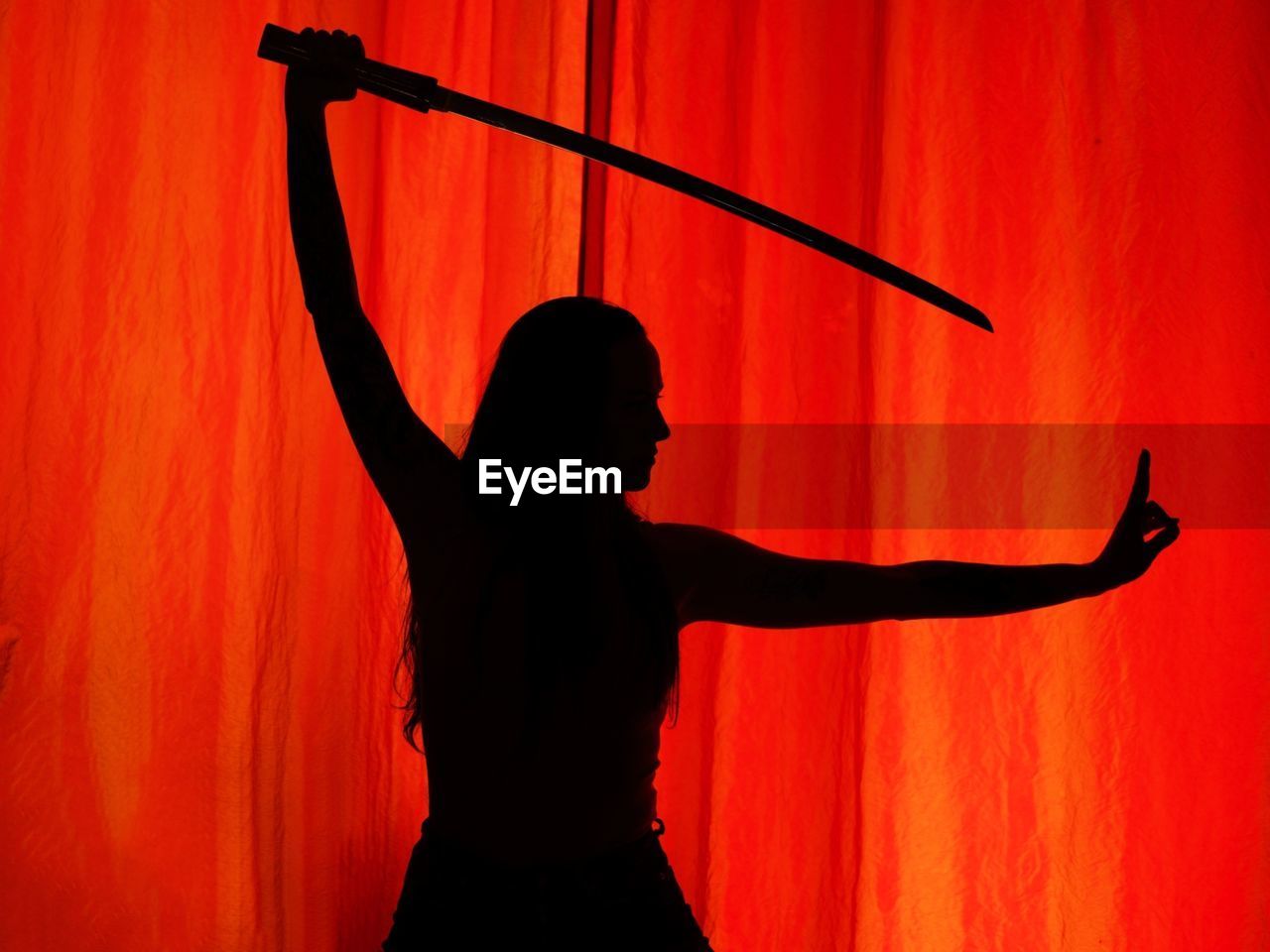 Shadow of woman with sword seen through red curtain