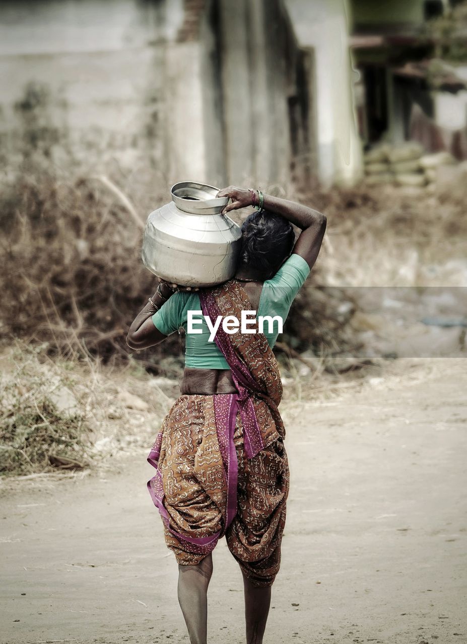 Rear view of woman carrying container on shoulder at road