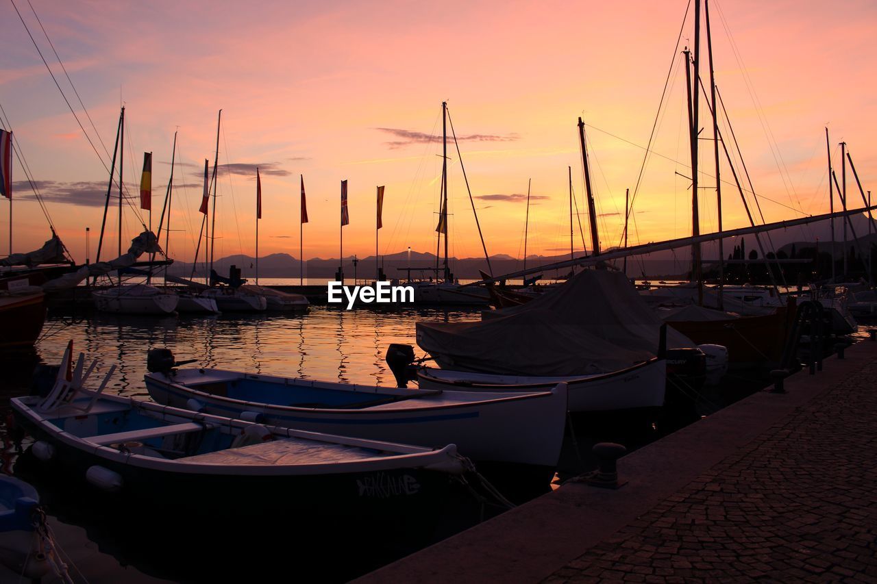 Sailboats moored at harbor during sunset