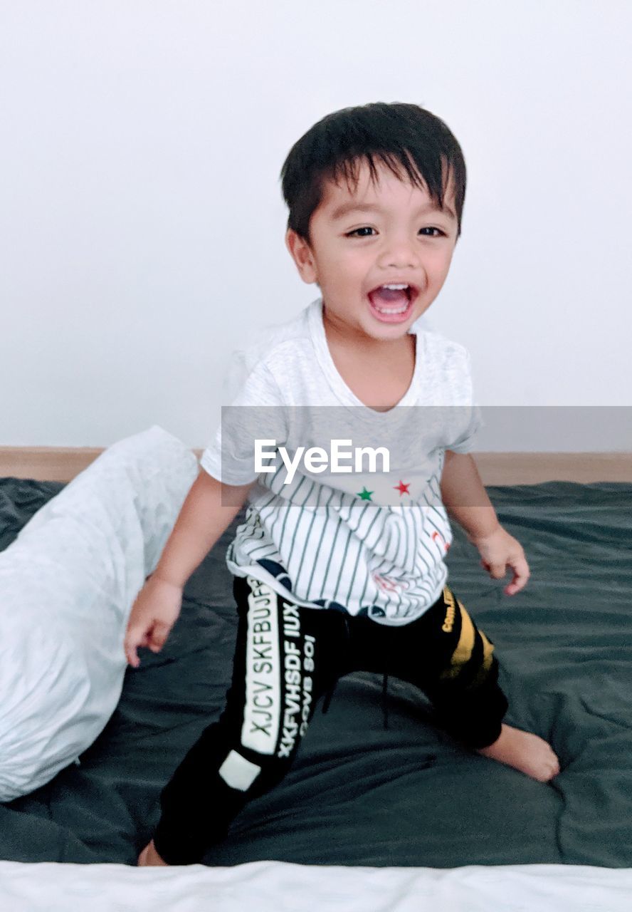 Portrait of cheerful boy standing on bed