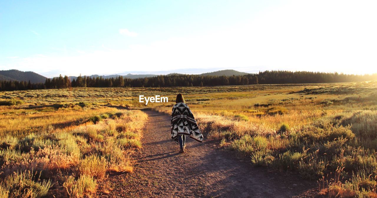 Rear view of woman waking on field against sky during sunset