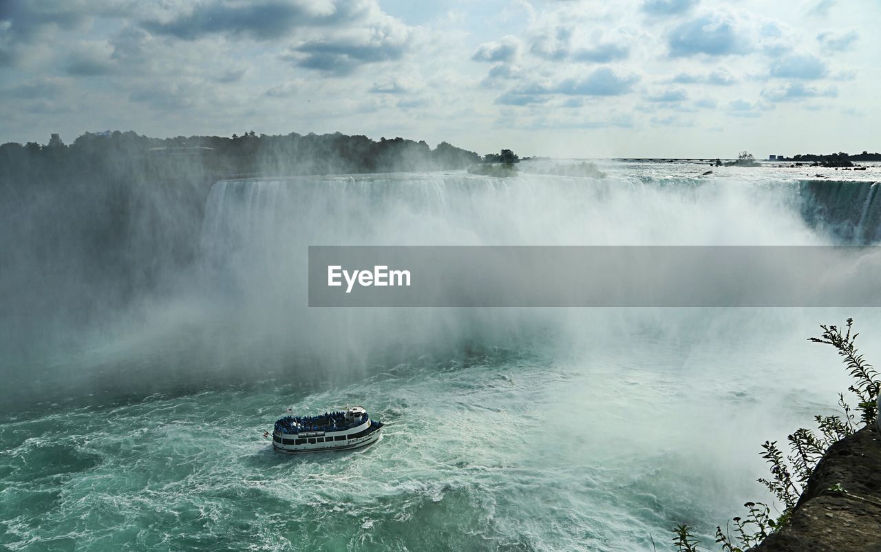 Ferry sailing in river by niagara falls against sky