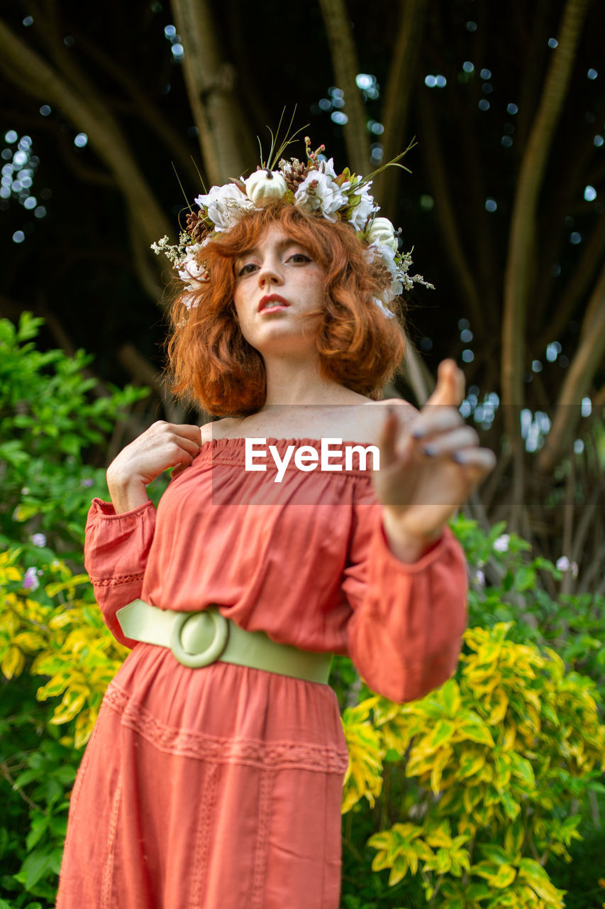 Portrait of woman wearing flowers while standing against trees