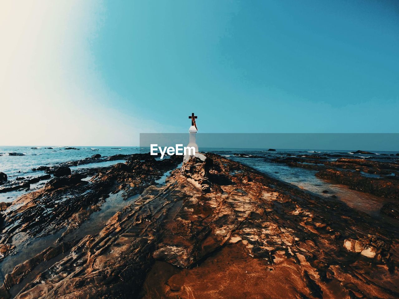 A christian cross on a rock by sea against clear sky