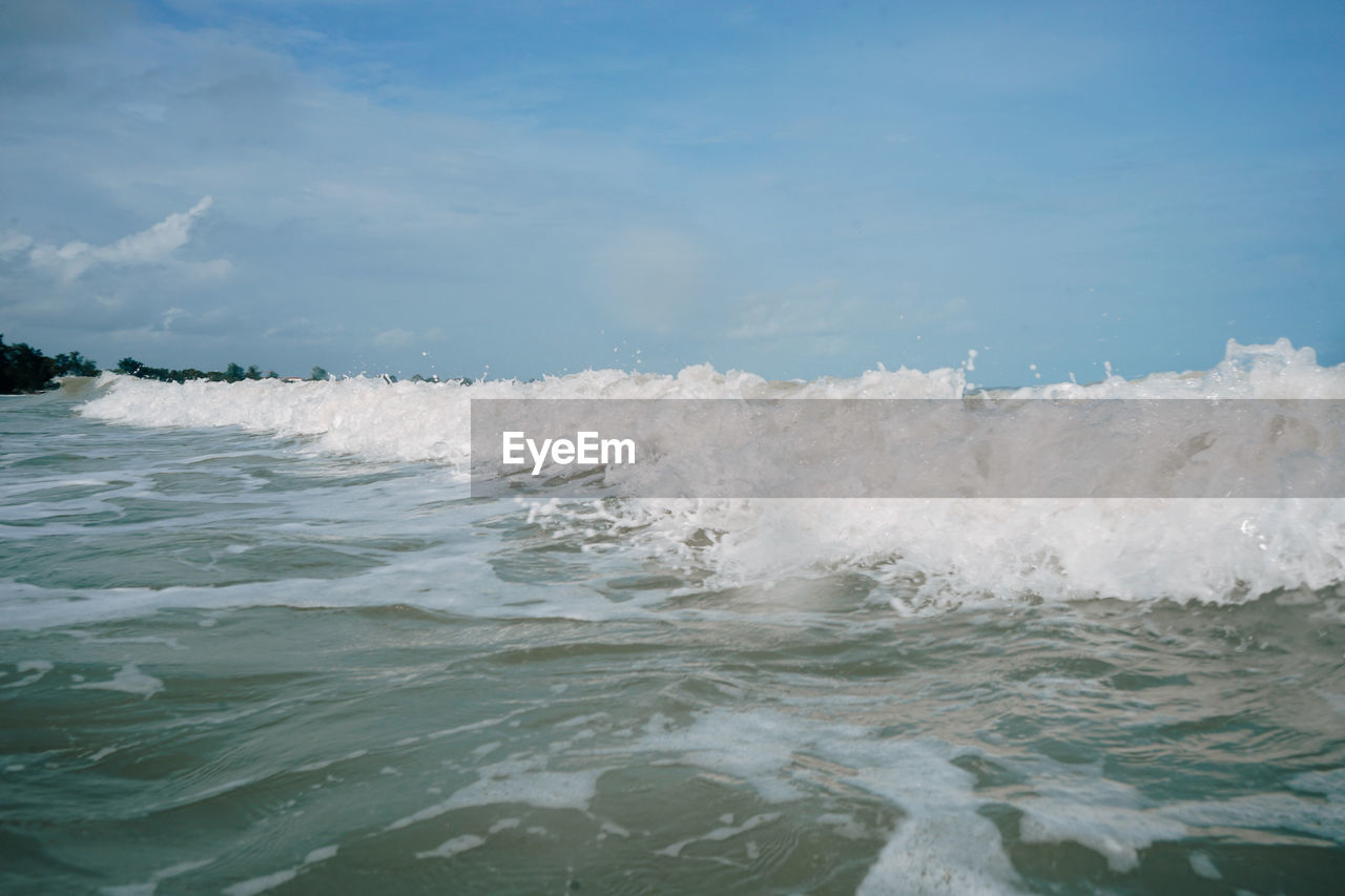 WAVES SPLASHING ON SHORE AGAINST BLUE SKY