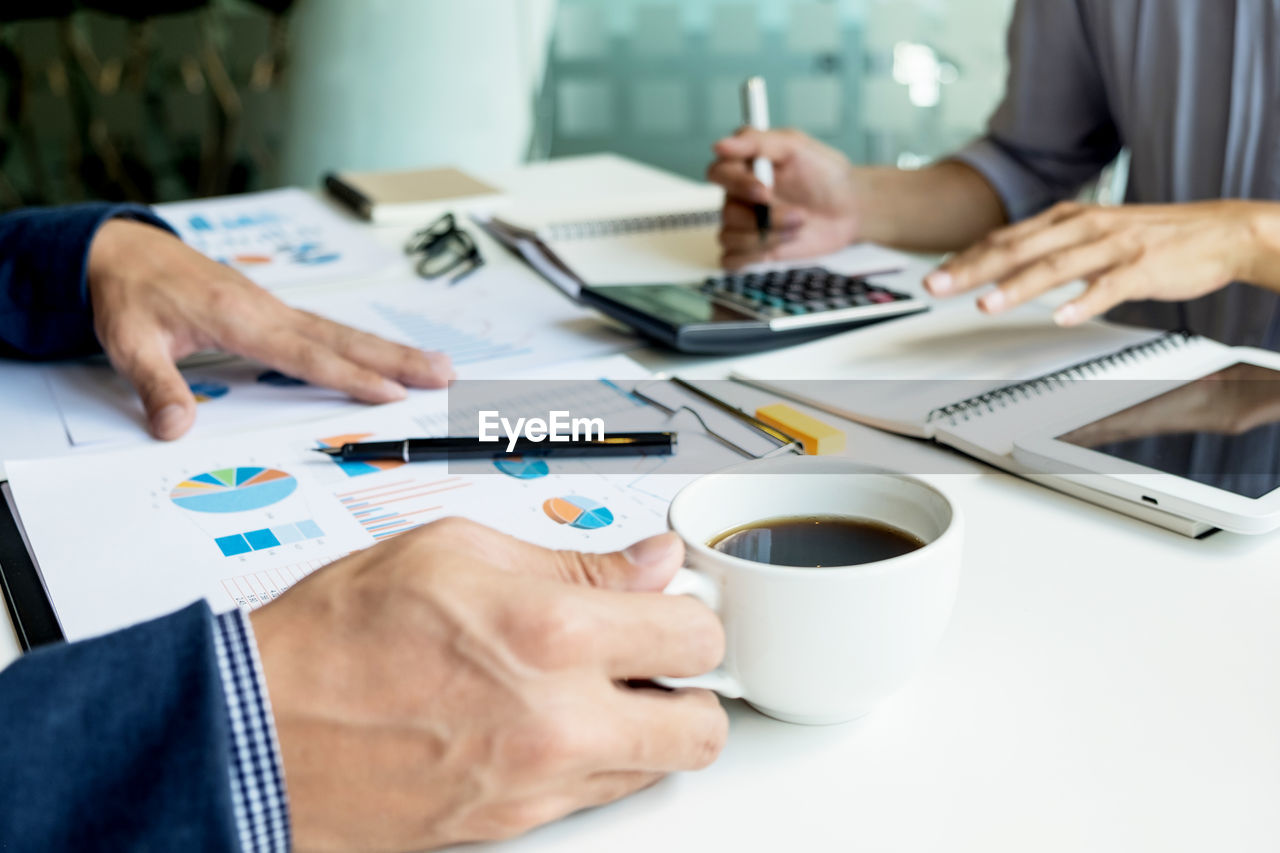 Cropped hand of businessman holding coffee while working with colleague in office