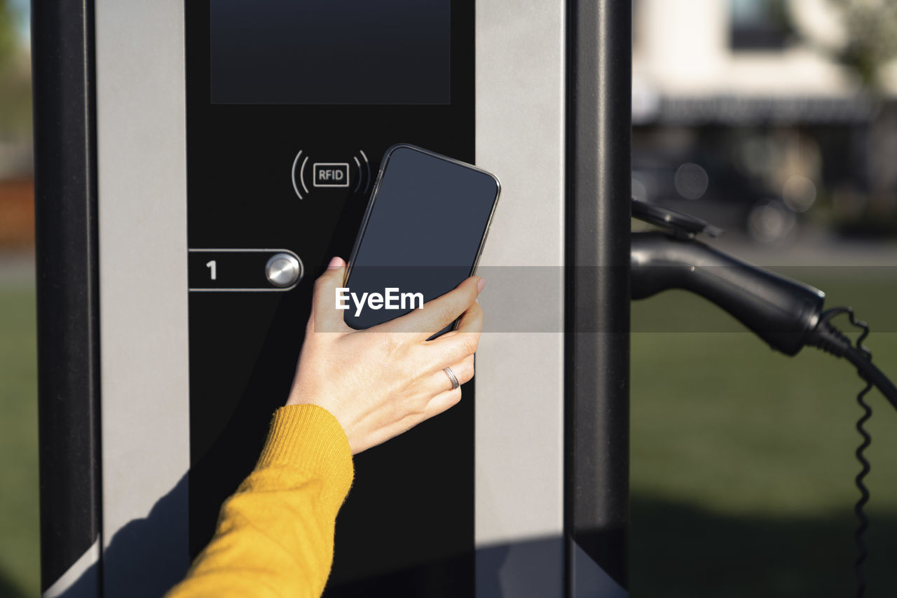 Hand of woman making payment through smart phone at vehicle charging station