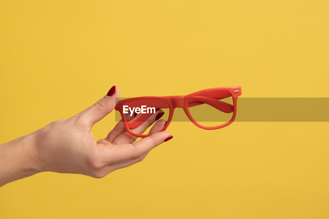 cropped hand of woman holding red heart shape against yellow background