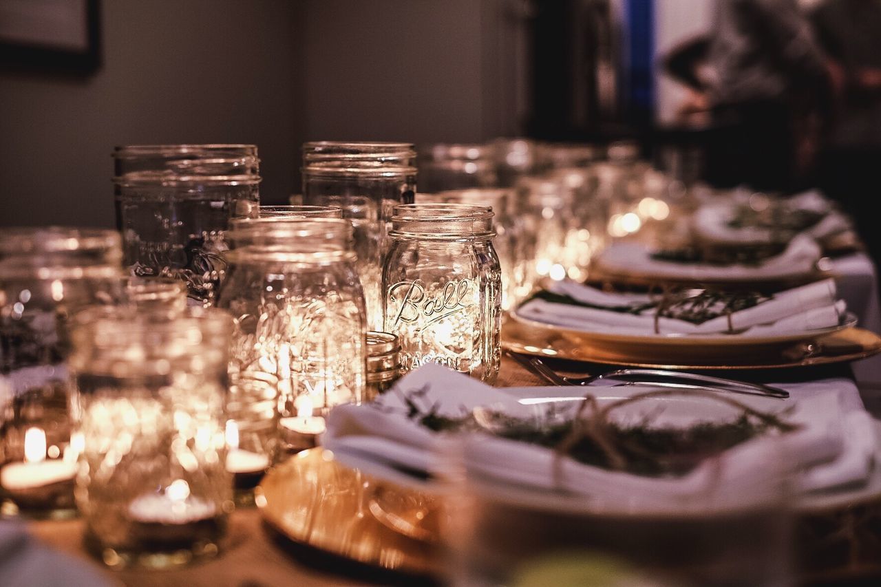 Tea light candles in glass jars by plates arranged on table