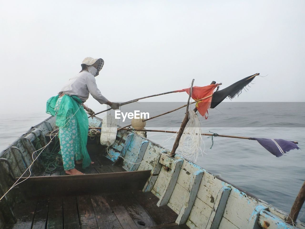 Woman fishing on boat in sea against clear sky