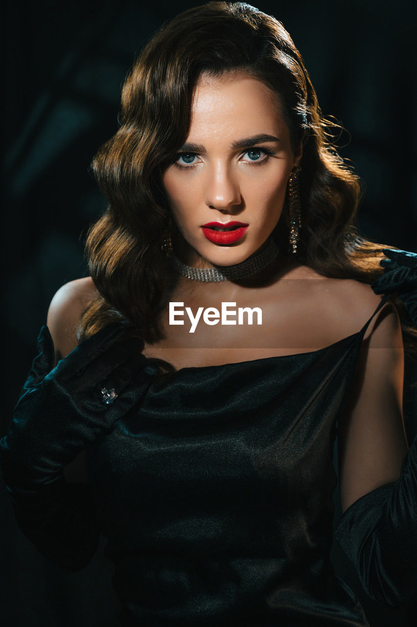 portrait of beautiful young woman standing against black background