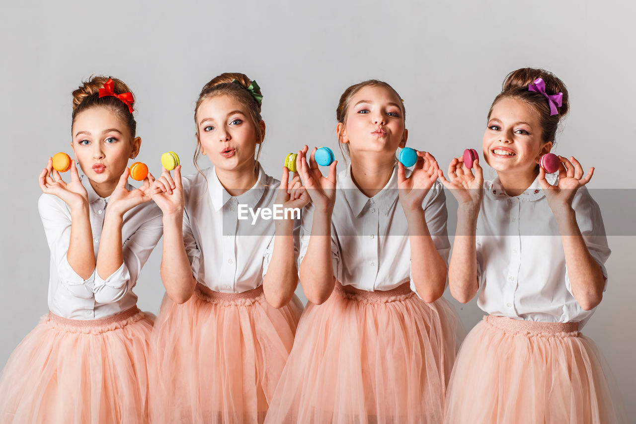 Portrait of girls holding colorful macaroons against white background