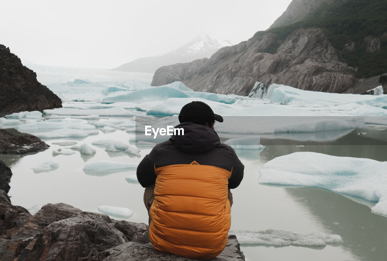 REAR VIEW OF WOMAN LOOKING AT LAKE AGAINST MOUNTAIN RANGE