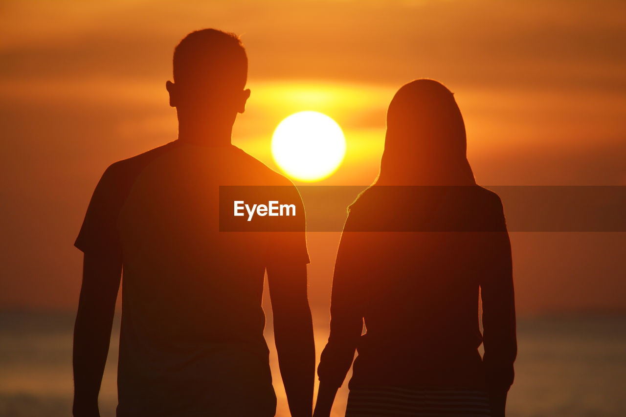 Rear view of couple at beach during sunset