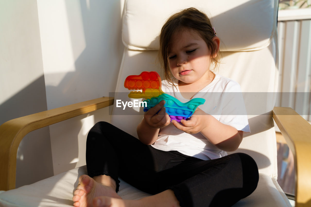 Girl holding toy while sitting on seat at home