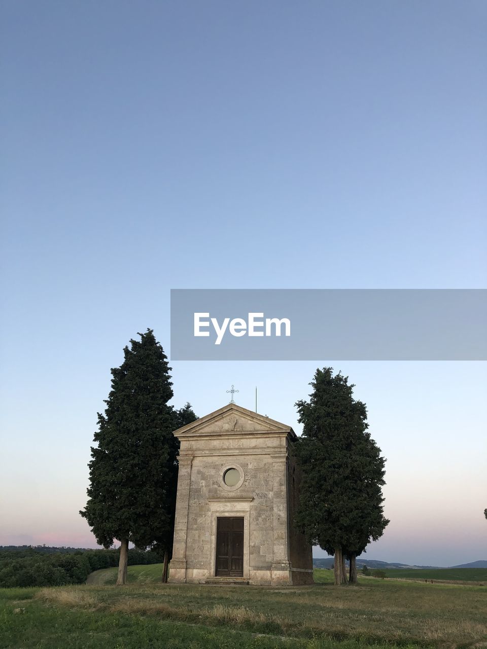 TREES ON FIELD BY BUILDING AGAINST SKY