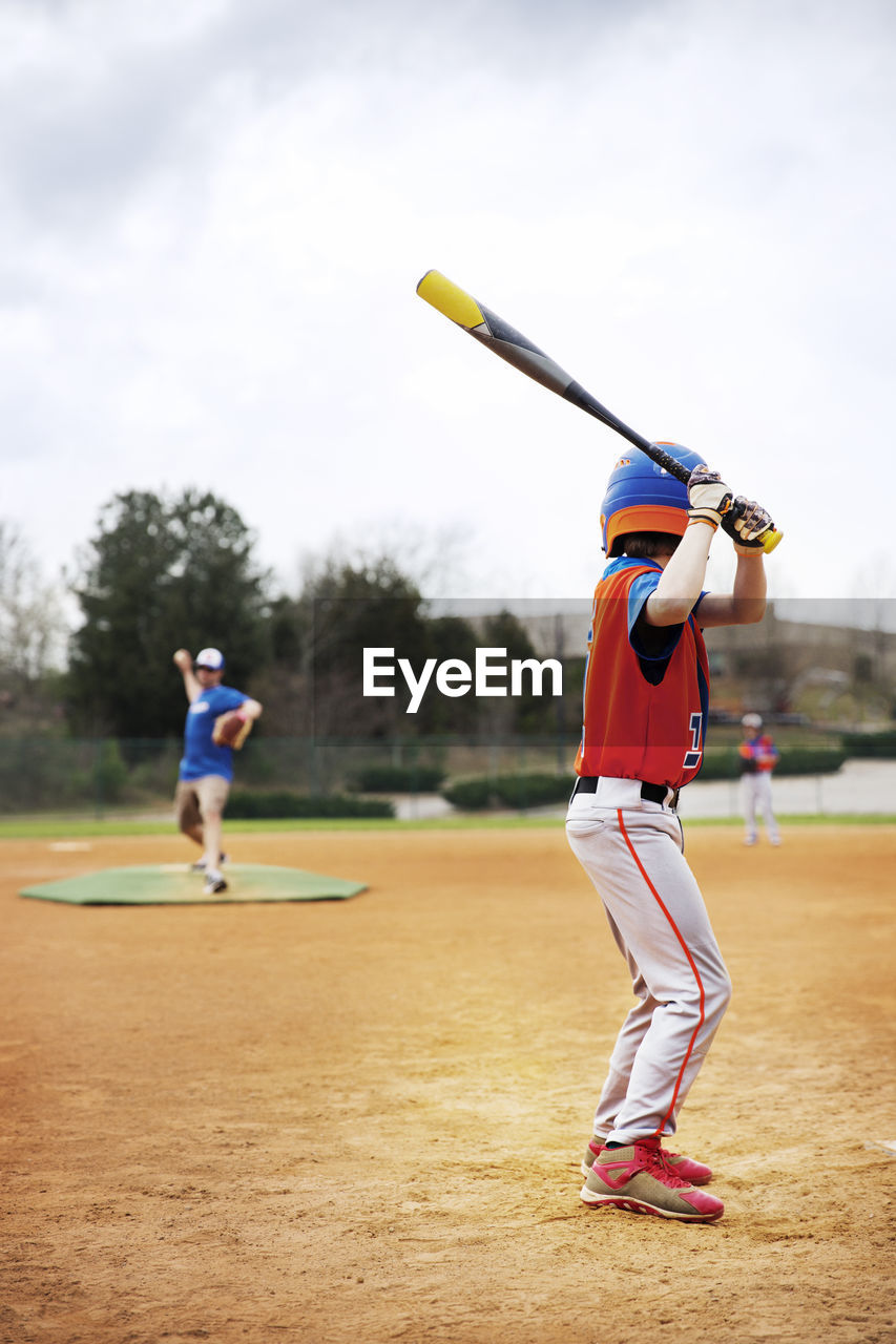 Side view of boy playing baseball with coach on field against sky