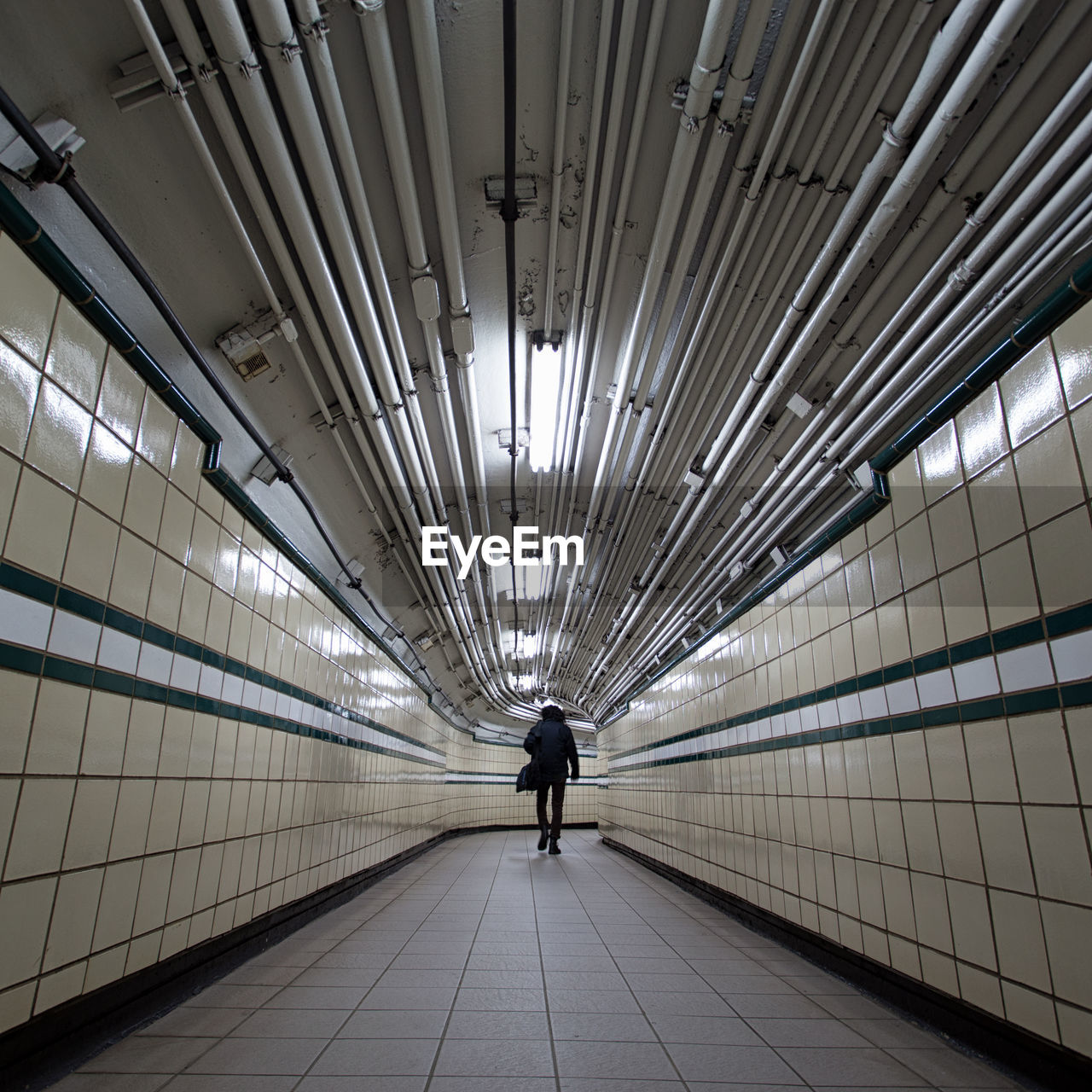 REAR VIEW OF WOMAN WALKING IN ILLUMINATED SUBWAY STATION