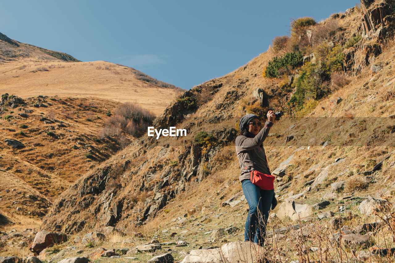 Rear view of man photographing on mountain against sky