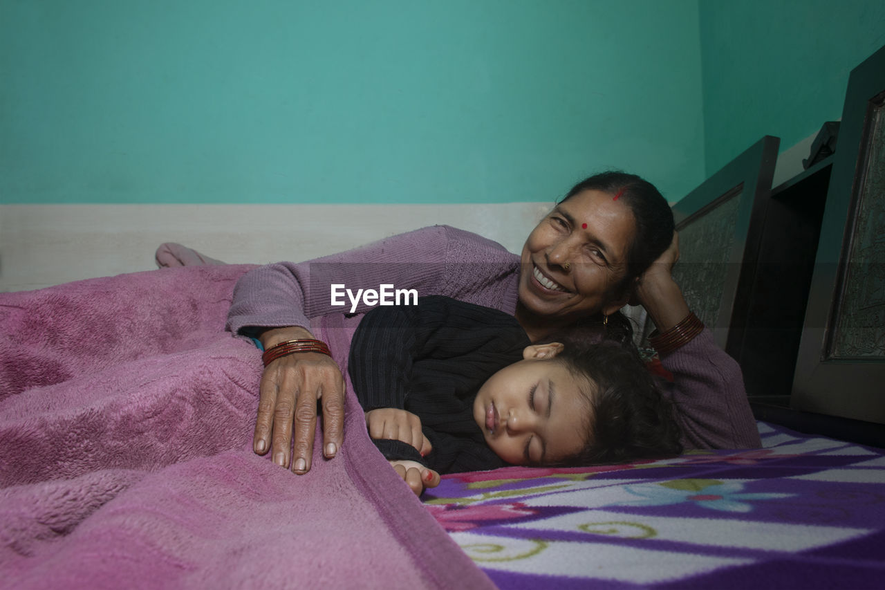 Portrait of grandmother with granddaughter sleeping on bed at home