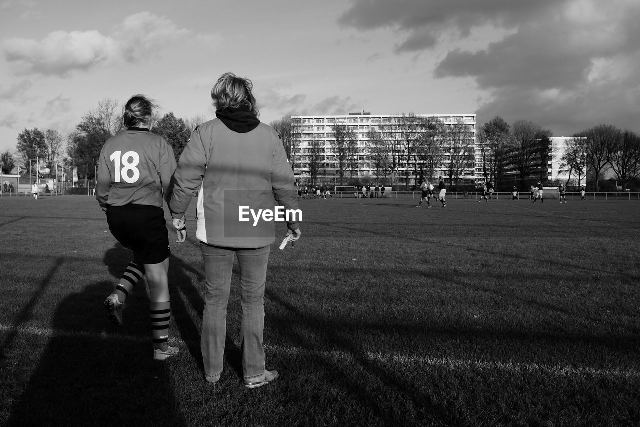 Rear view of coach with soccer player standing on field against sky