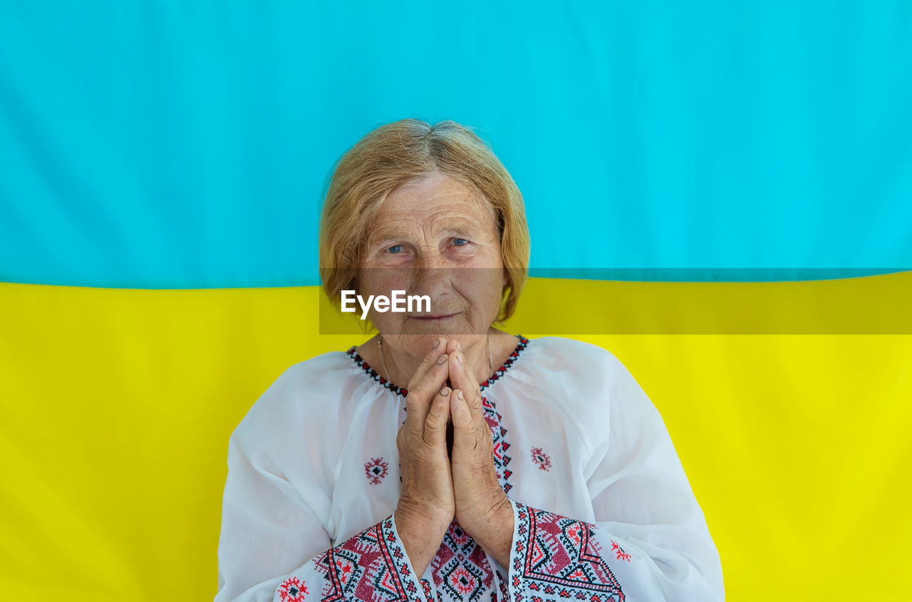 Senior woman with hands clasped against ukrainian flag