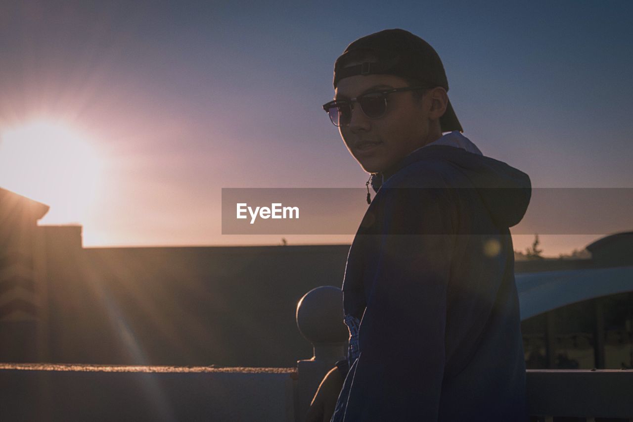 Low angle view of man wearing sunglasses by railing against sky during sunset