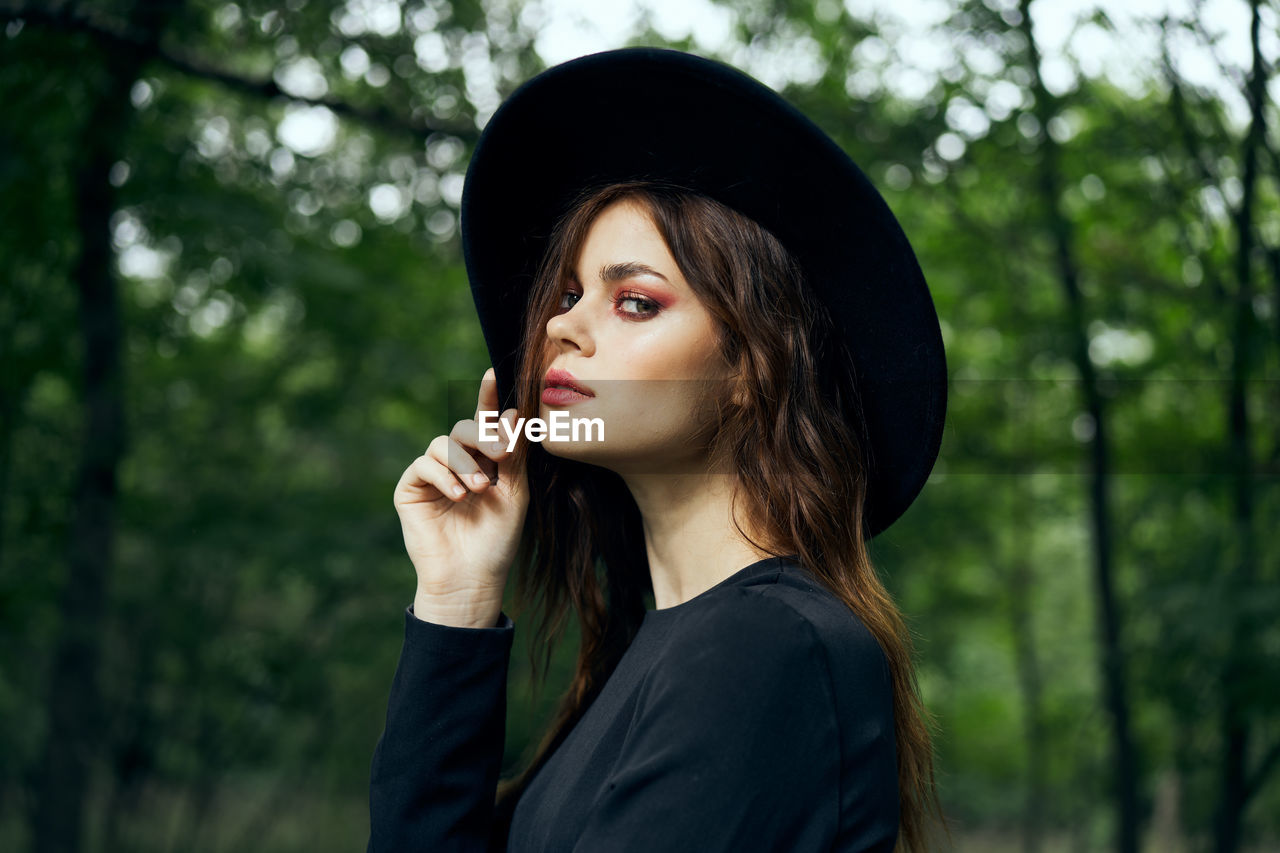 portrait of young woman standing against trees