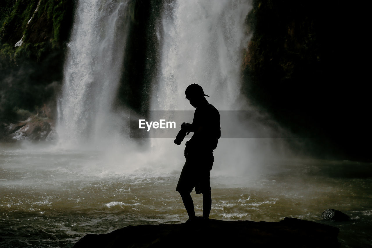 Silhouette man standing against waterfall