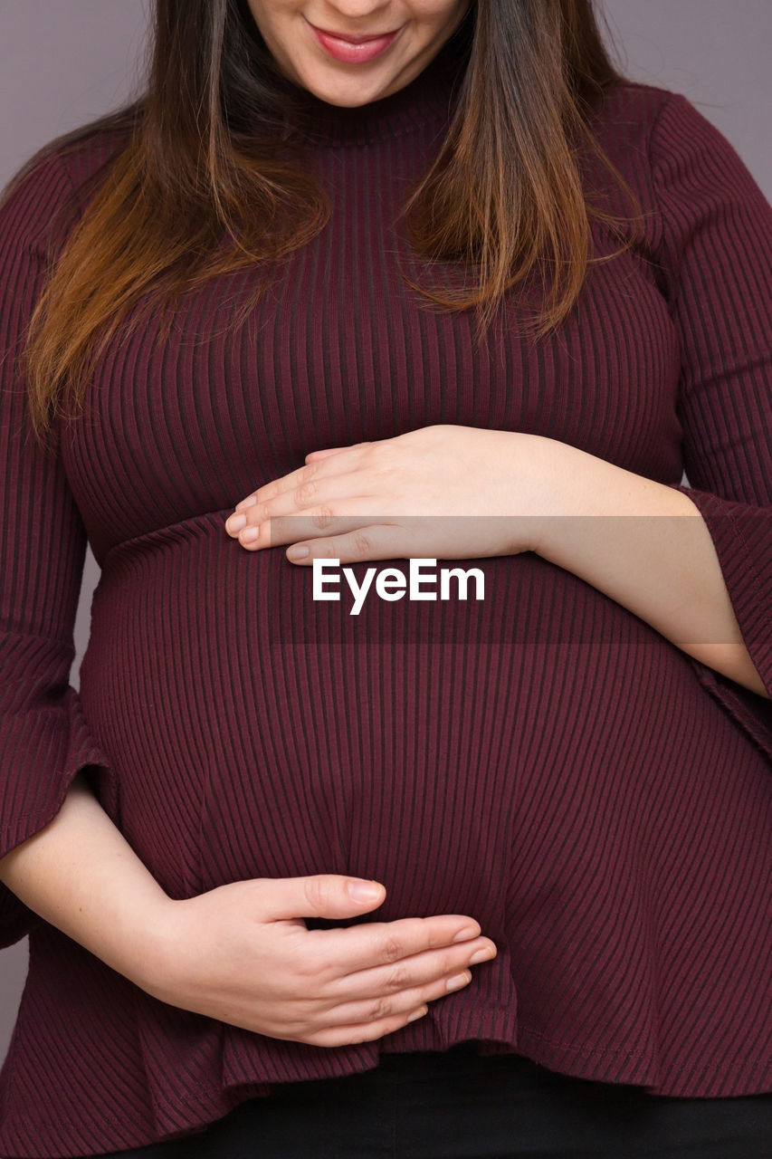 Midsection of smiling pregnant woman touching abdomen