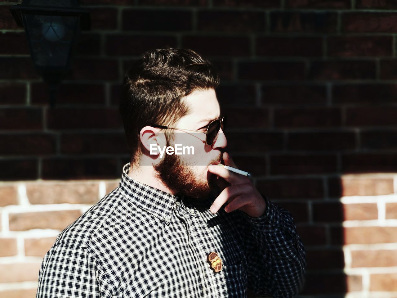 Young man looking away while smoking cigarette against brick wall