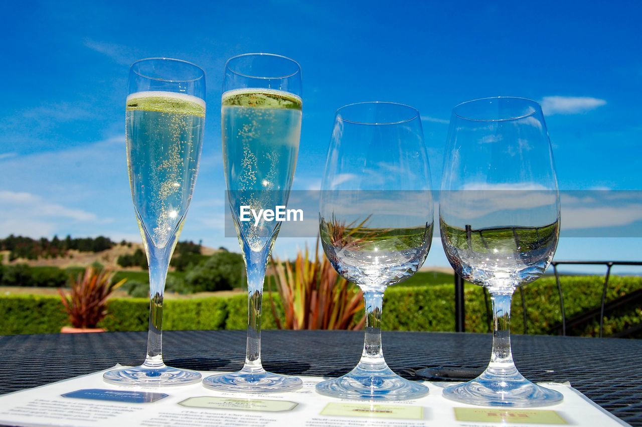Low angle view of wineglass and champagne flutes on table against blue sky
