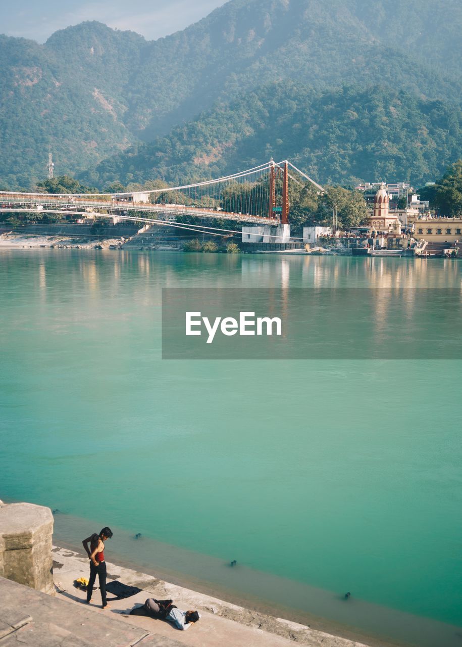 HIGH ANGLE VIEW OF BRIDGE OVER SEA AGAINST MOUNTAINS