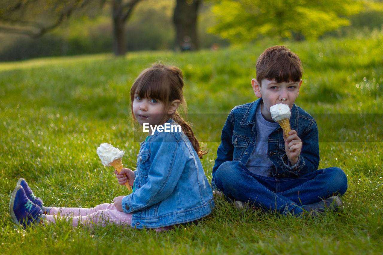 Two children sitting on grass eating ice cream
