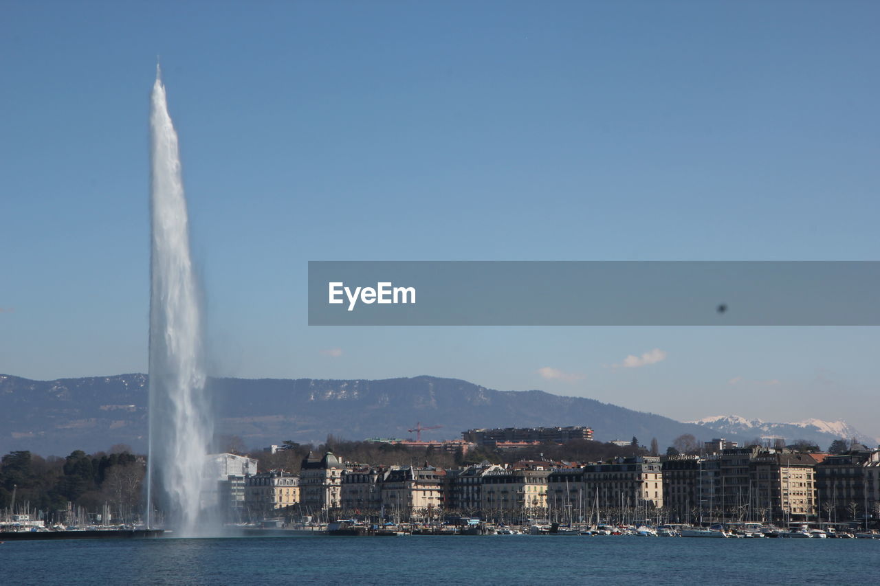 Waterfront scenic view of fountain in city against sky