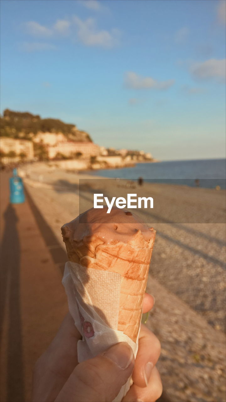 Close-up of hand holding ice cream at beach against sky