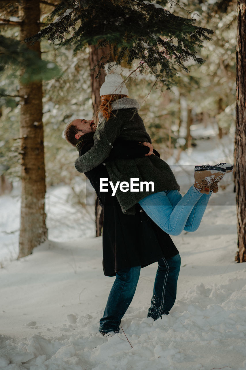 Couple embracing while standing on snow covered land