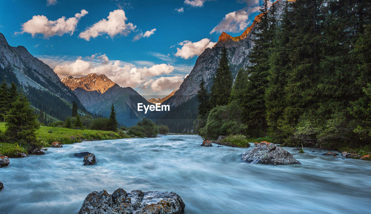 Scenic view of stream flowing through rocks against sky